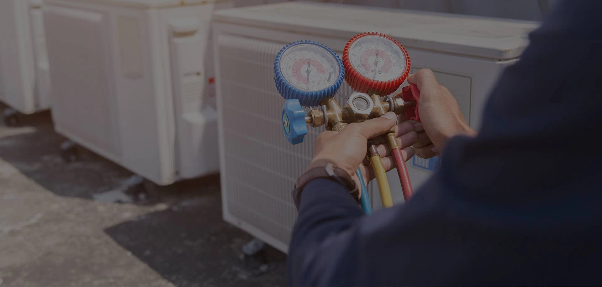 A person holding two gauges in front of an air conditioner.