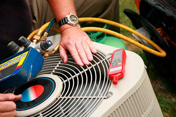 Air conditioning contractor servicing an air conditioning unit with tools and gauges.