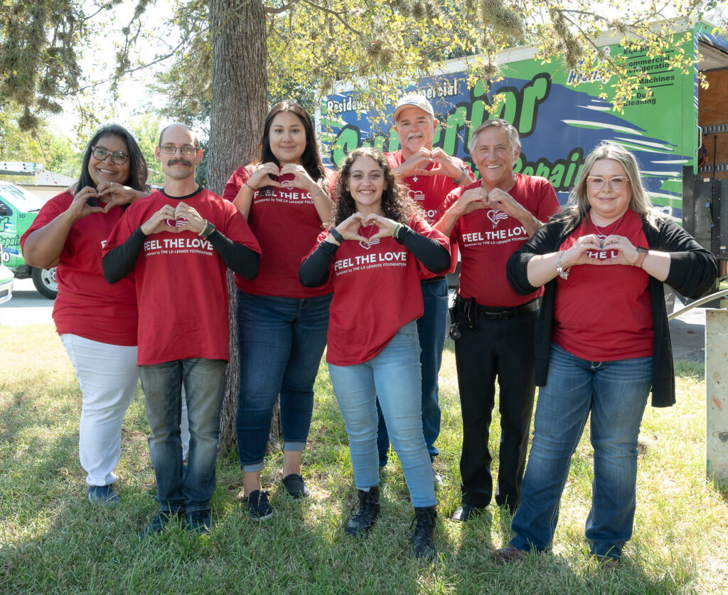 A group of people standing in the grass holding up heart signs.