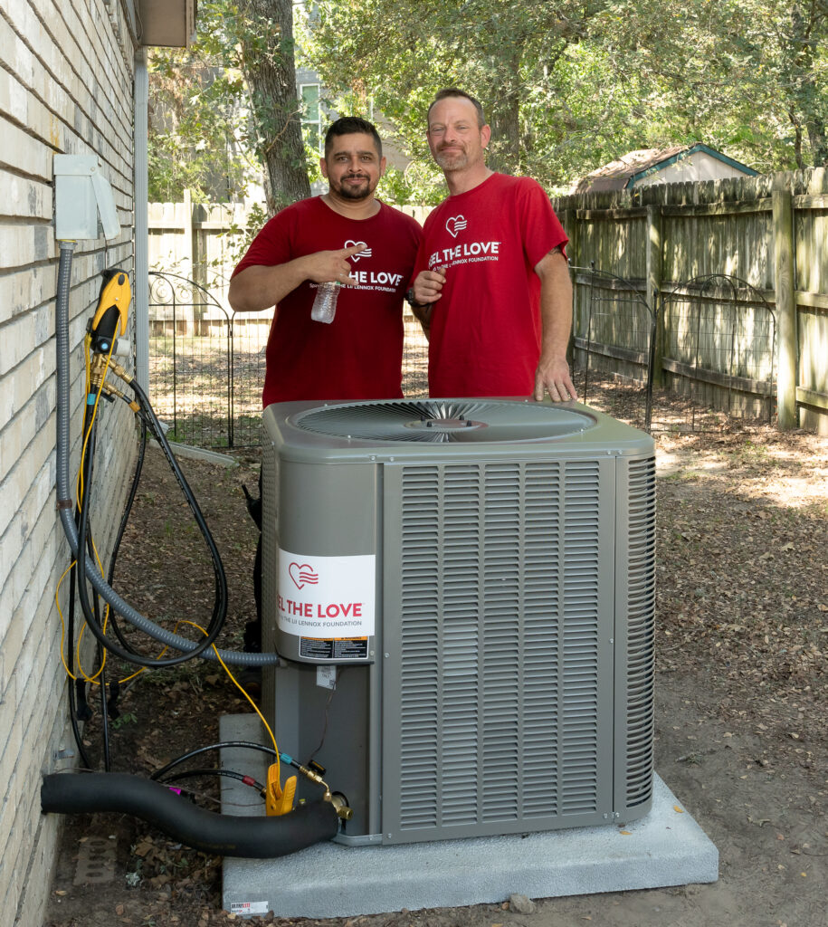 Two men standing next to a residential air conditioner.